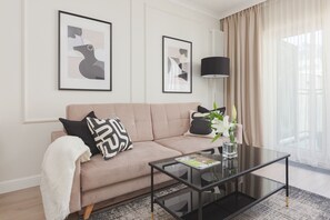 nother angle of the living room, showcasing a wide view with a beige sofa, a dining table with chairs, and large windows with curtains letting in natural light.