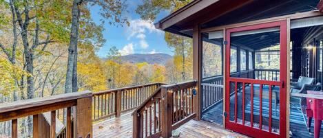 The Blue Ridge mountains stretch majestically in the distance. From the cozy cabin deck, the view is breathtaking, with vibrant autumn foliage coloring the foreground. The tranquil scene invites contemplation and relaxation in the heart of nature.