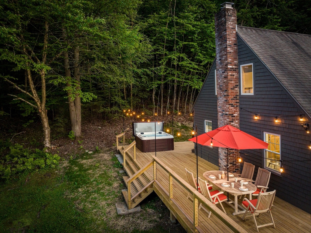 A Stowe, Vermont vacation home with a spacious deck, hot tub, table and chairs surrounded by woods