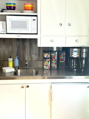 Counter and sink with mini fridge, microwave, toaster and coffee supplies.