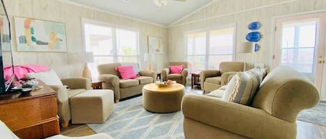 Comfortable living room with ceiling fans, large windows, and sky-blue ceiling. 