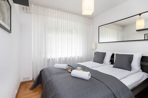 Cozy bedroom with a double bed, soft gray bedding, and bright curtains for a relaxing ambiance.
