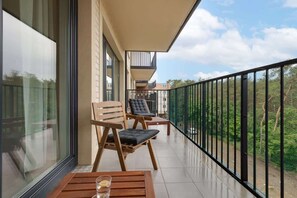A balcony with a small table and two chairs offers a scenic view of the surrounding greenery and hills. Ideal for relaxing and enjoying the fresh air.