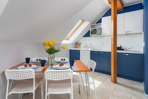 A bright dining area with a white table and chairs, situated next to a fully equipped kitchen with blue and white cabinets.