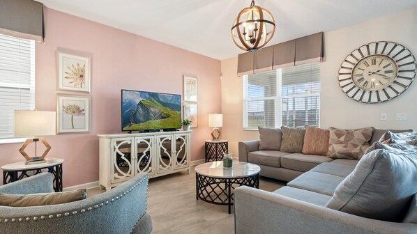 Chic living room with soft pastel accents, cozy seating, and TV!