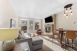 Cozy living area with mounted flat screen TV, gas fireplace, queen sleeper sofa, and balcony access.