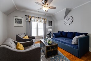 Living room includes a second television, daybed, closet and club chairs.