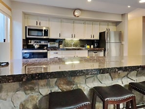 The eat-in bar serves as an ideal bridge between the kitchen and living area and provides easy dining, snacking and serving. Note the fabulous stone work, granite countertops and stainless steel appliances that elevate the space.