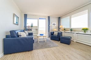 Gesamteindruck Wohnzimmer mit Sofa, Sessel, Essplatz und Austritt zur Südloggia