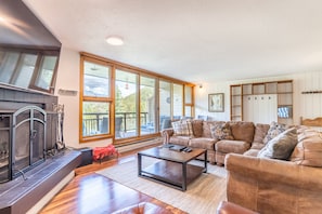 Spacious living area with large mounted flat screen TV, hardwood flooring, access to the private balcony, wood burning fireplace and ample seating.