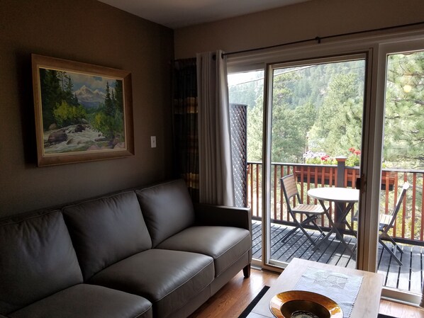 living room opens to deck with flower box, table and chairs, awning, and patio