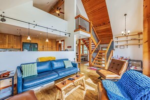 Charming Open-Concept Living Space with Vaulted Ceilings, Hardwood Floors, and an Inviting Staircase Leading to a Loft Area