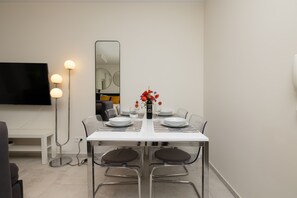 A dining area with a white table and chairs, set for four people with flowers as a centerpiece.