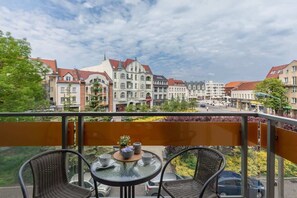 A beautiful balcony with a round table and chairs, overlooking a charming waterfront with historic buildings in the background.

