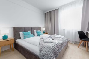A cozy bedroom featuring a large bed with a tufted headboard, soft gray bedding, and elegant curtains, creating a tranquil retreat.

