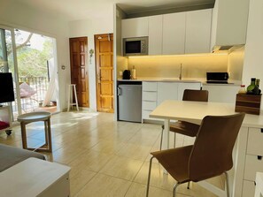 The bright and airy living space features a modern, fully equipped kitchen with white cabinets and a sleek countertop, perfect for preparing delicious meals during your stay. The tiled floors add a touch of elegance, while the sliding glass doors offer br