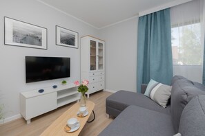 A living area with a mounted TV, white cabinets, and a gray couch. The space is cozy and well-lit with simple decor.