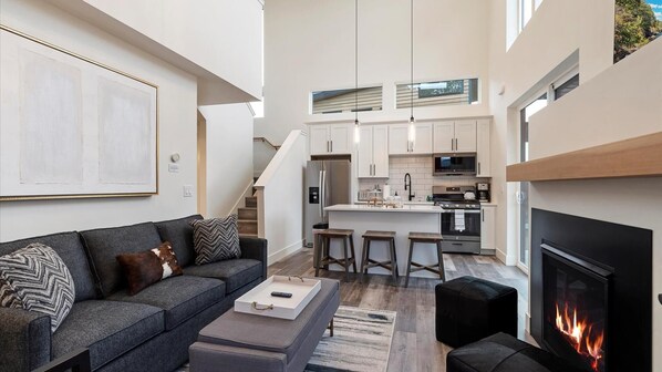 Open concept living room, dining area, and fully stocked kitchen. The living room features vaulted ceilings, a luxury queen sofa sleeper, HDTV with cable and streaming, gas fireplace, and breakfast bar seating for 3.