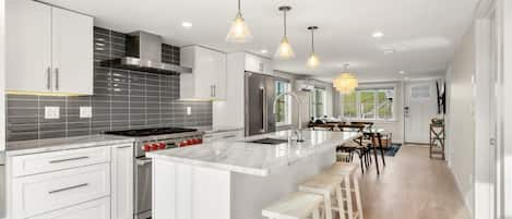 Fully equipped open kitchen and living room with large island, high-end appliances, kitchen table, washer/dryer, smart tv