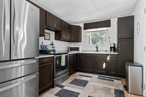 Our kitchen boasts elegant dark wooden hanging cabinets, a sunlit sink in front of a window, and cozy rugs. It's the perfect blend of style and comfort.