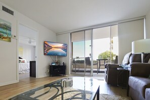The bright and airy living room offers plush seating, a mounted TV, and floor-to-ceiling windows leading to a spacious patio with tropical views.