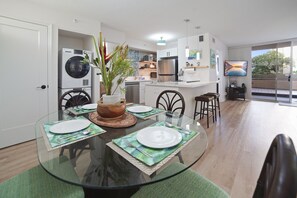 Enjoy a spacious open-concept dining and living area with a glass-top table, tropical decor, and a seamless flow to the kitchen and patio. Ideal for family gatherings!