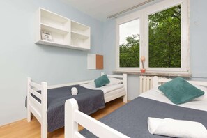 Functional bedroom with two single beds with white wooden frames, a shelf hangs above one of the beds.