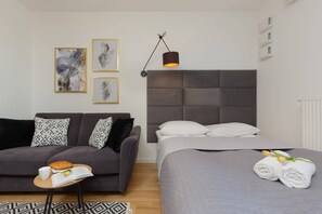 Another perspective showing the bedroom area with a double bed with a soft upholstered headboard, next to the bed there is a gray sofa bed The whole is cozy and functional.