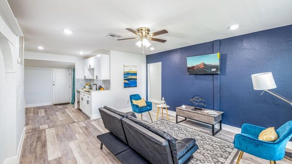 This small living room features a comfortable couch, a TV for your entertainment, and a ceiling fan to keep the space cool.