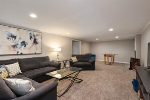 The lower level features an additional lounge space that doubles as a game room, providing ample space for everyone to unwind.