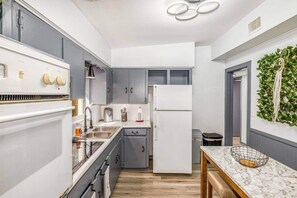 Kitchen with oven, sink, refrigerator, storage cabinets, knife set, paper napkins, deep fryer, trash cans, dining table