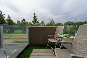 A balcony with artificial grass flooring, outdoor seating, and a scenic view of trees in the distance.