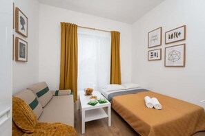 A cozy bedroom area with a wooden table, mustard yellow curtains, and a TV mounted on the wall.
