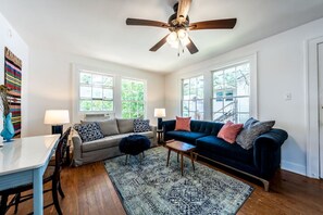 Comfy living room with large velvet couch, queen sleeper sofa, plus a desk with a TV with streaming platforms(Please note that we've added nice curtains since this photo was taken for filtering light + adding privacy)