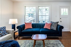 Comfy living room with large velvet couch, queen sleeper sofa, plus a desk with a TV with streaming platforms(Please note that we've added nice curtains since this photo was taken for filtering light + adding privacy)