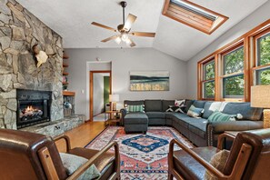 Family room features a stone fireplace with gas logs, vaulted ceiling, and skylight, and XX" smart TV.