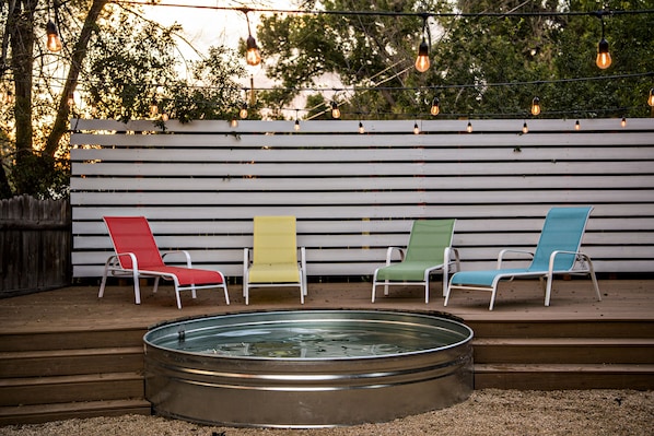 Stock tank pool at sunset, lounge chairs market lights.