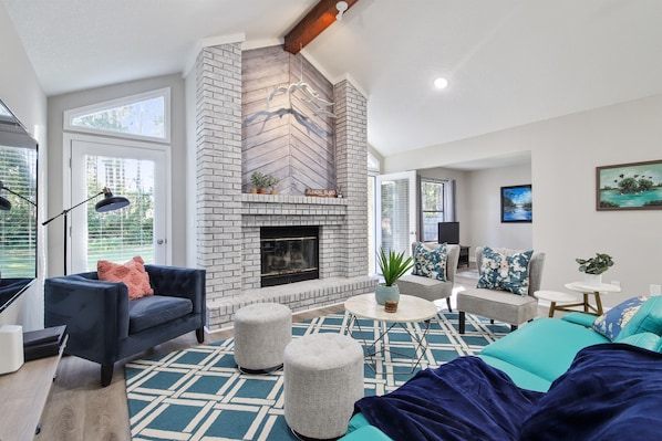 You will feel so relaxed in this bright and airy living room.  The view of the greenery outside adds to the open feel of the home. Original midcentury modern leather sofa and seagulls flying over the mantel add style to this fantastic space.