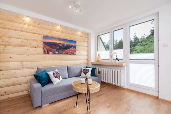 A cozy living room featuring a plush blue sofa with decorative cushions, a round wooden coffee table, and a scenic painting on the wall, creating a warm and inviting atmosphere.