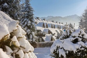 A breathtaking winter scene of snow-covered rooftops and trees, with majestic mountains in the background, evoking a serene and peaceful vibe.