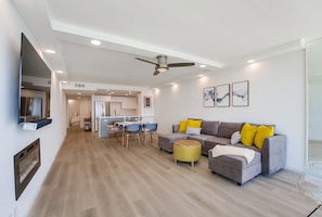 Living space includes sofa, electric fireplace, ceiling fan, smart TV, dining table for 4-6, fully equipped kitchen with stainless steel appliances, breakfast bar with 2 stools and bedroom and bathroom toward the front of the unit