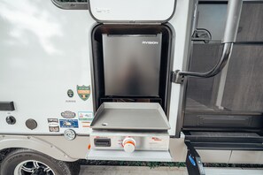 The outdoor kitchen is equipped with a mini refrigerator, spray port, & griddle