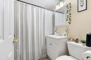 Cozy full bathroom with tub designed with style, high pressure detachable handheld shower head , mounted shampoo, conditioner, and body wash on the shower wall, including plenty of supplies under the sink.