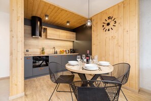 A kitchenette with a wooden dining table and modern black chairs. A clock decorates the wall, adding charm.