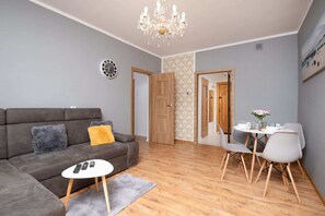 The living room is illuminated by a classic chandelier, with a grey sofa and stylish decor. The wooden door adds a natural element.