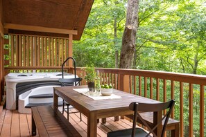 Upper deck features a hot tub with views of the surrounding forest and an outdoor dining area.