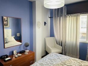 Habitación de matrimonio con butaca blanca, tocador y espejo.