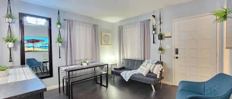 Shared room with sofa, dining table, decorations with artificial plants, exterior windows with curtains, mirror, main access door