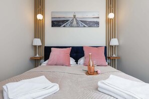 A cozy bedroom with a pink and white color palette, a double bed, and modern lighting.
