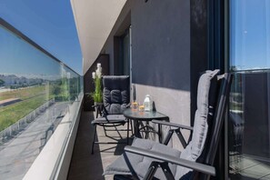 A balcony with outdoor seating, overlooking a contemporary building and greenery.